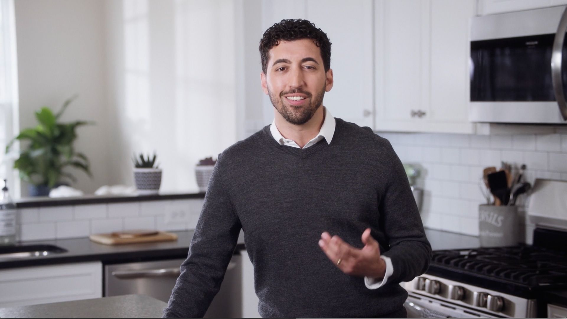 A man in a gray sweater is standing in a kitchen.