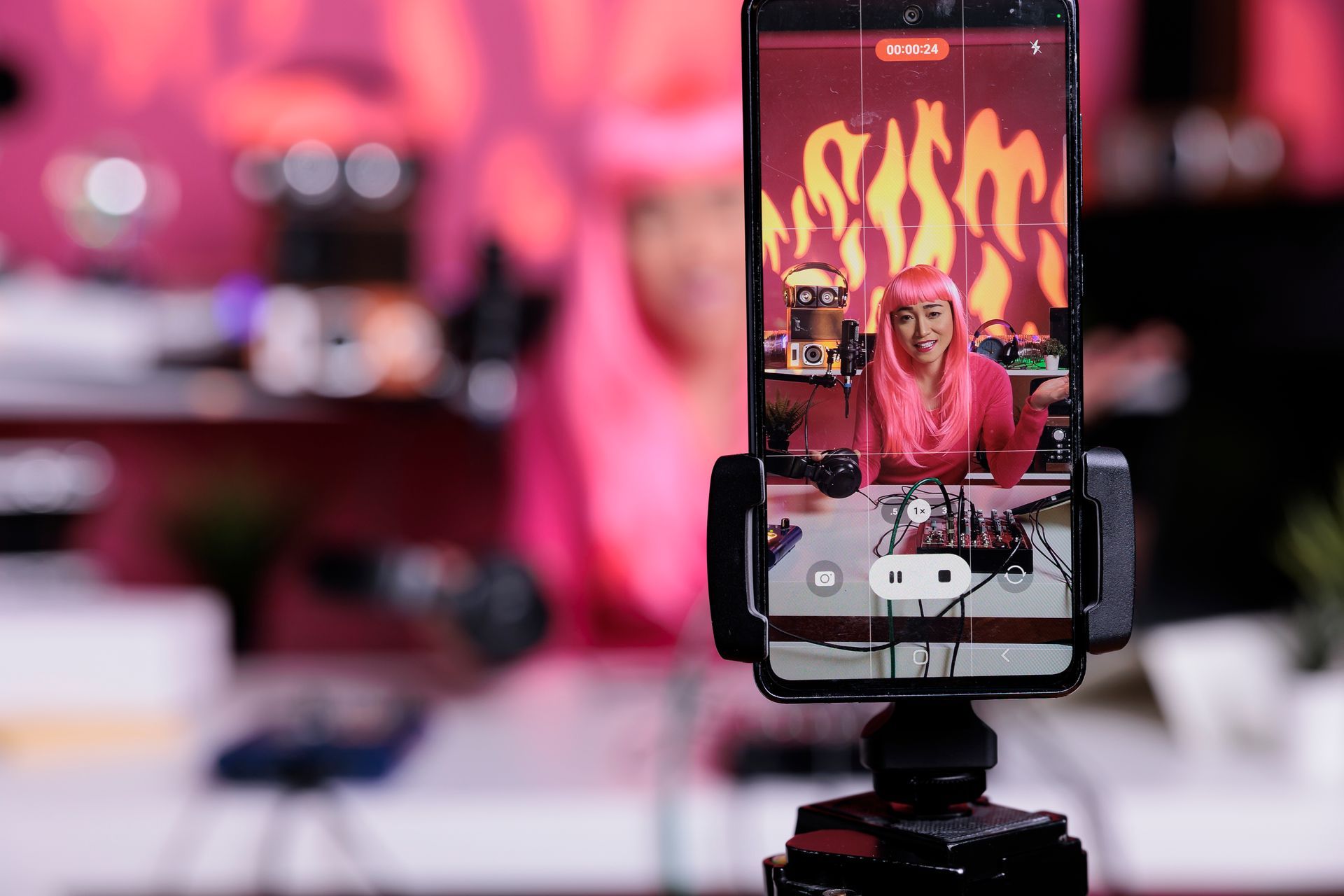 A woman with pink hair is being filmed on a cell phone on a tripod.