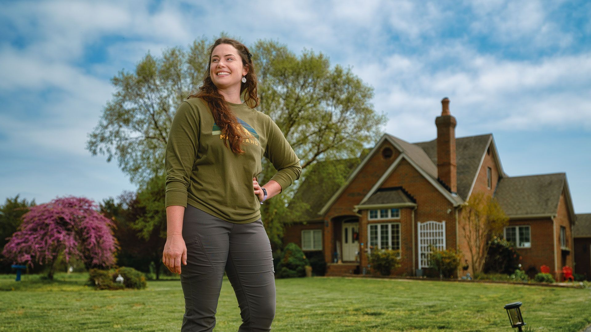 A woman is standing in front of a large brick house.