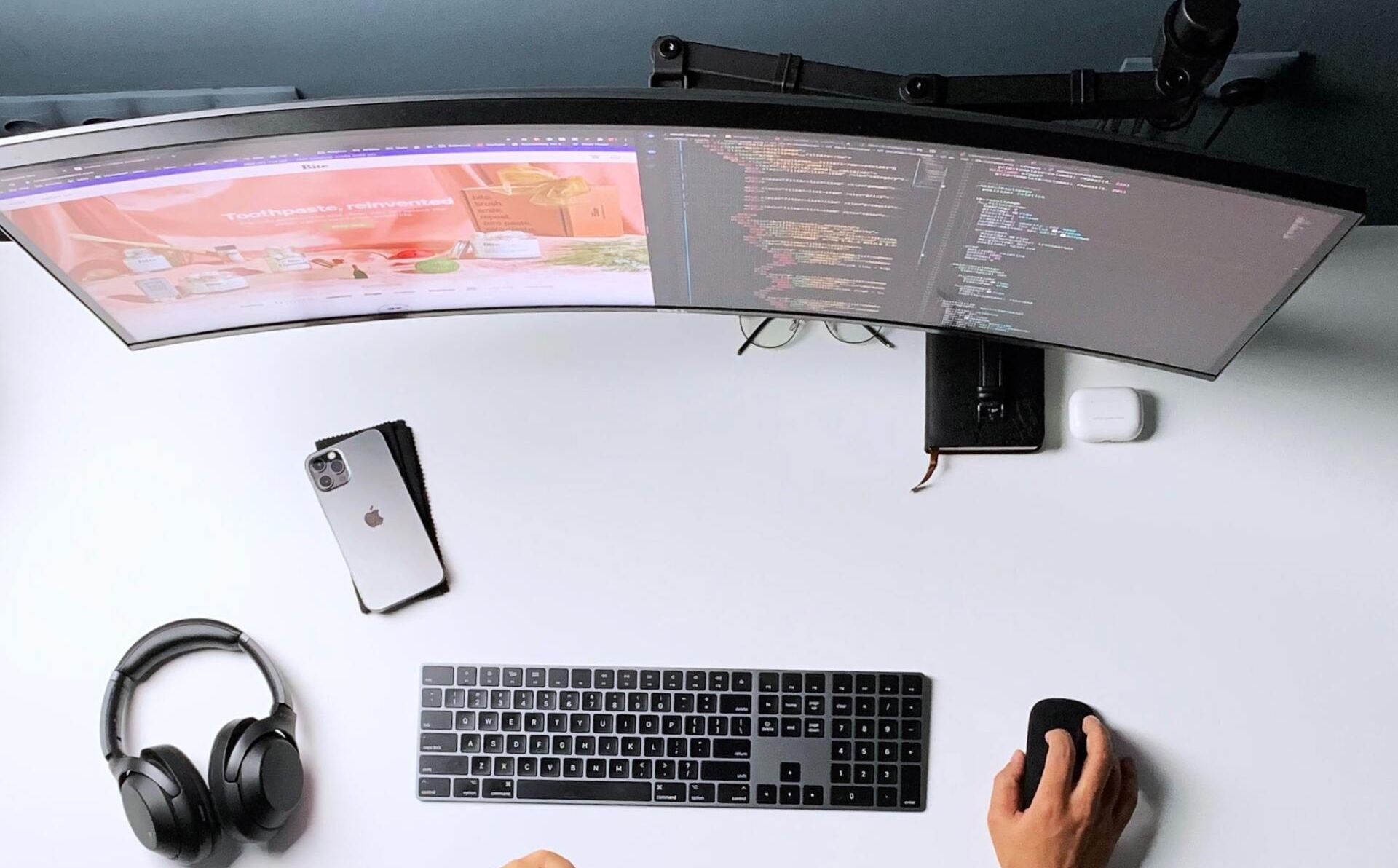 A person is sitting at a desk with a computer , keyboard , mouse and headphones.