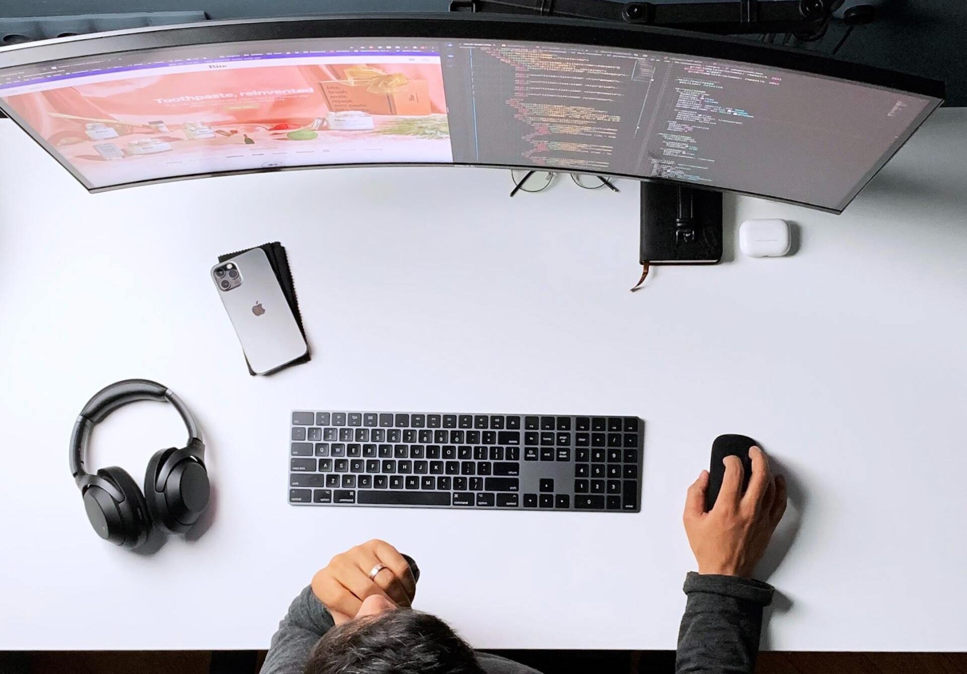 A person is sitting at a desk with a computer , keyboard , mouse and headphones.