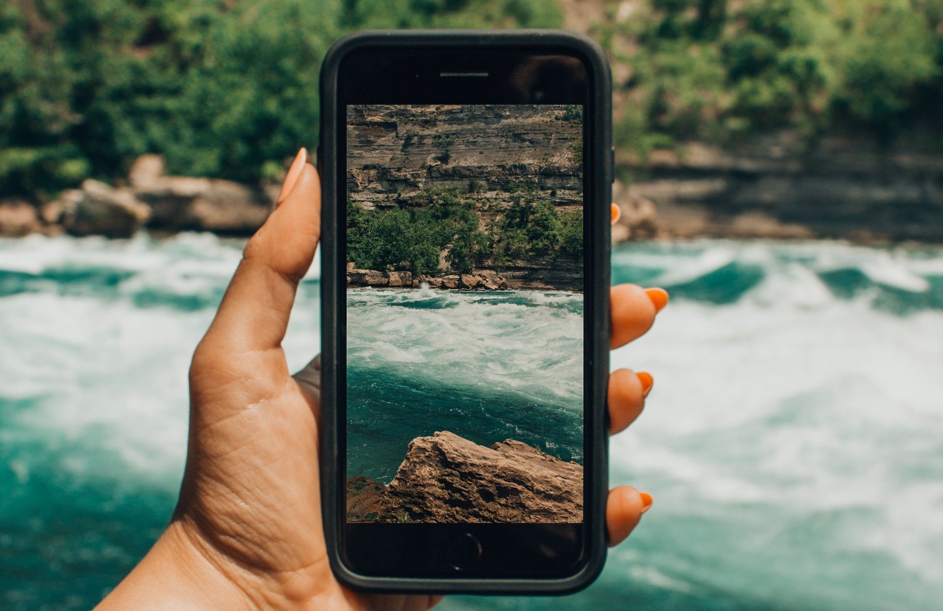 A person is holding a cell phone with a picture of a waterfall on it.