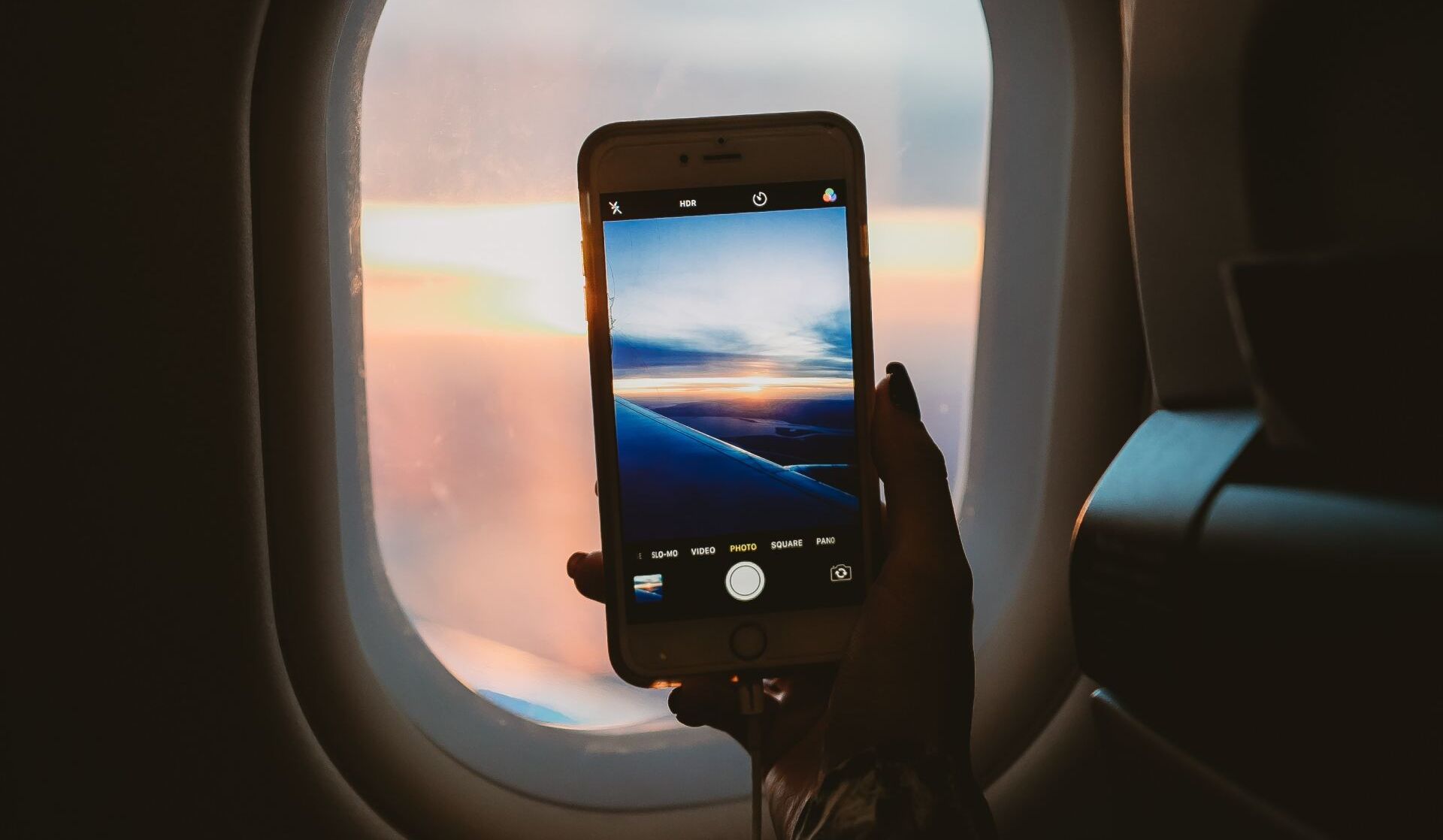 A person is holding a cell phone in front of an airplane window.