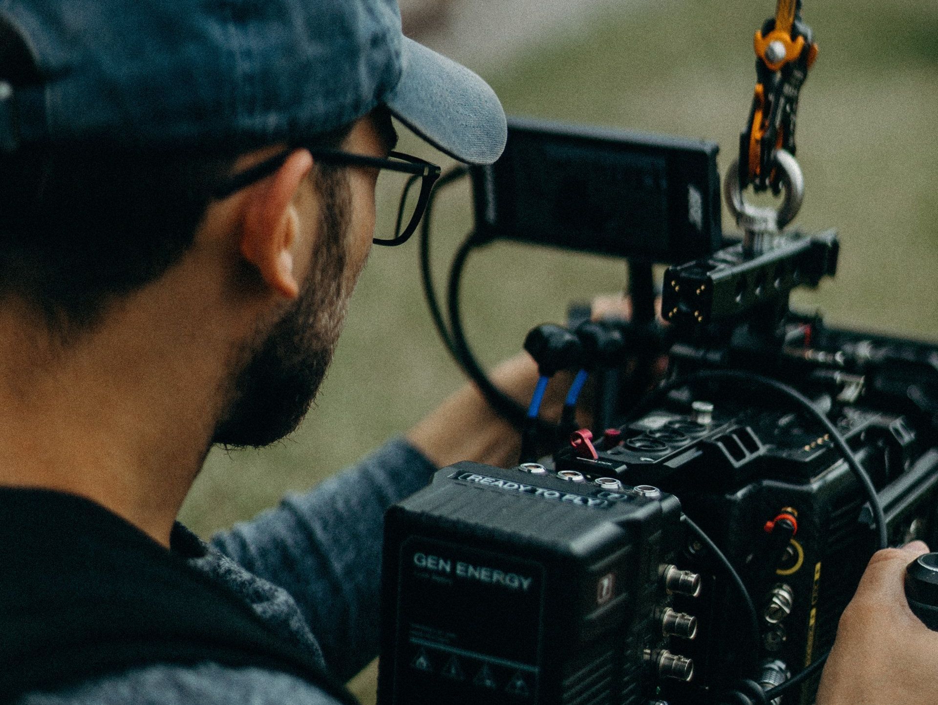 A man is holding a camera in his hands while wearing a hat and glasses.