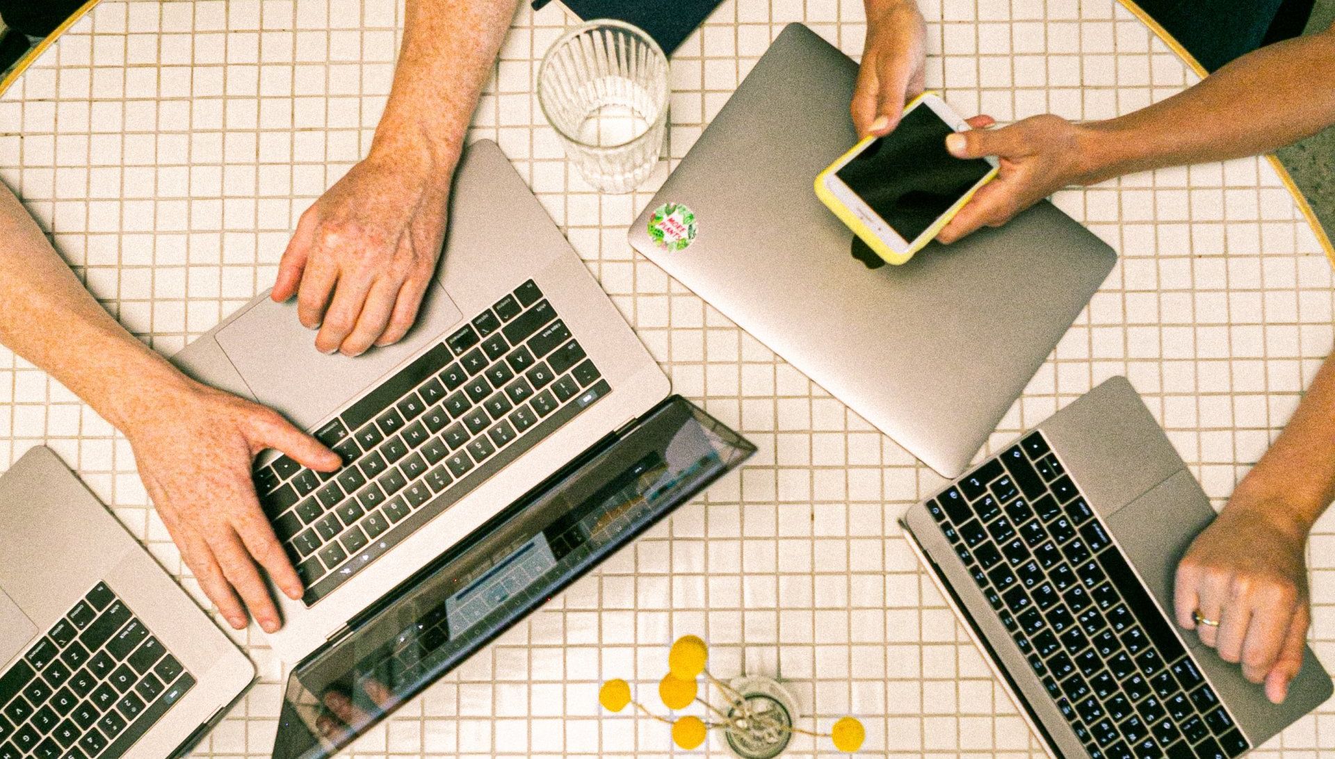 A group of people are sitting at a table with laptops and a cell phone.