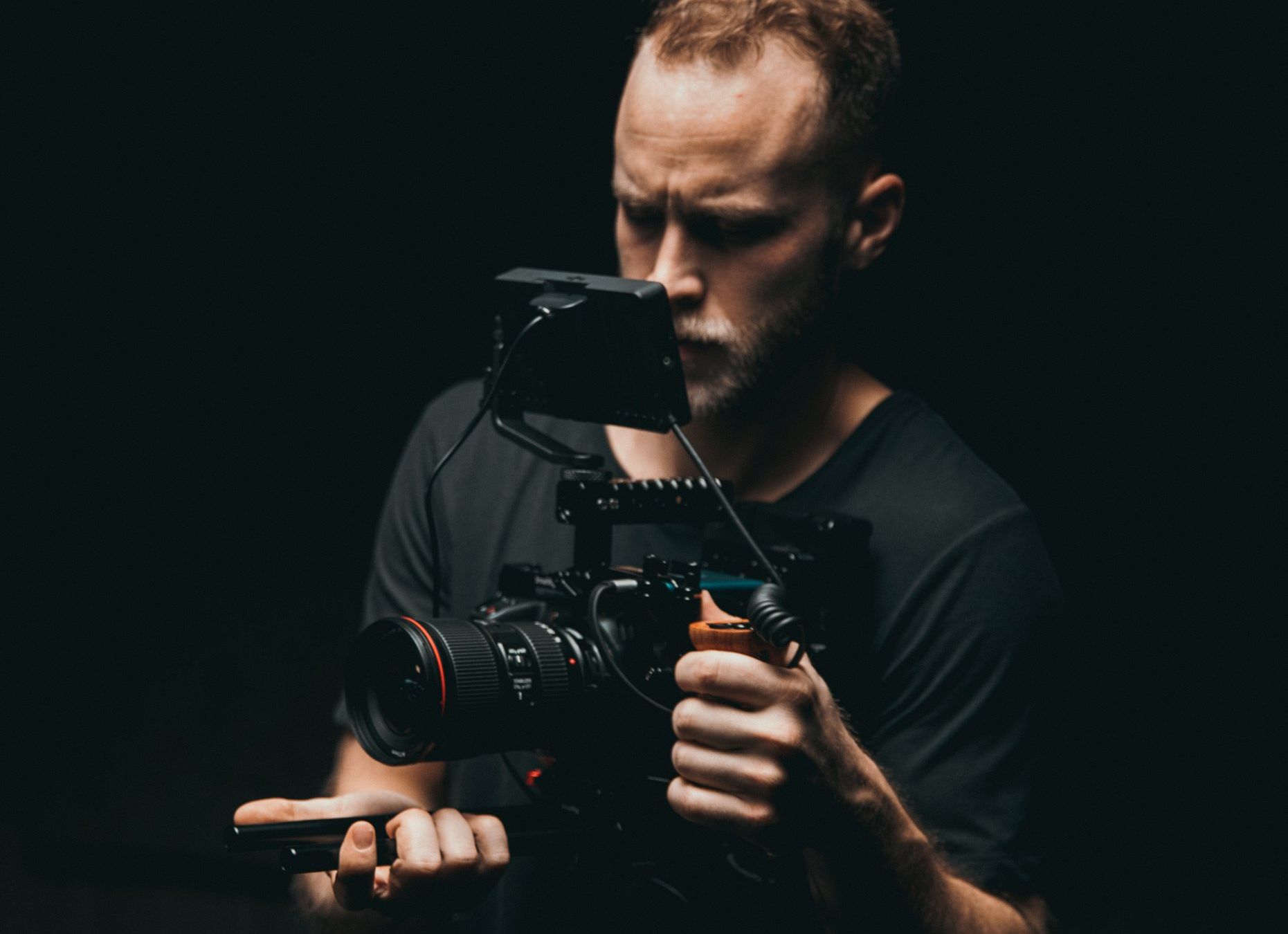 A man is holding a camera in his hands in a dark room.