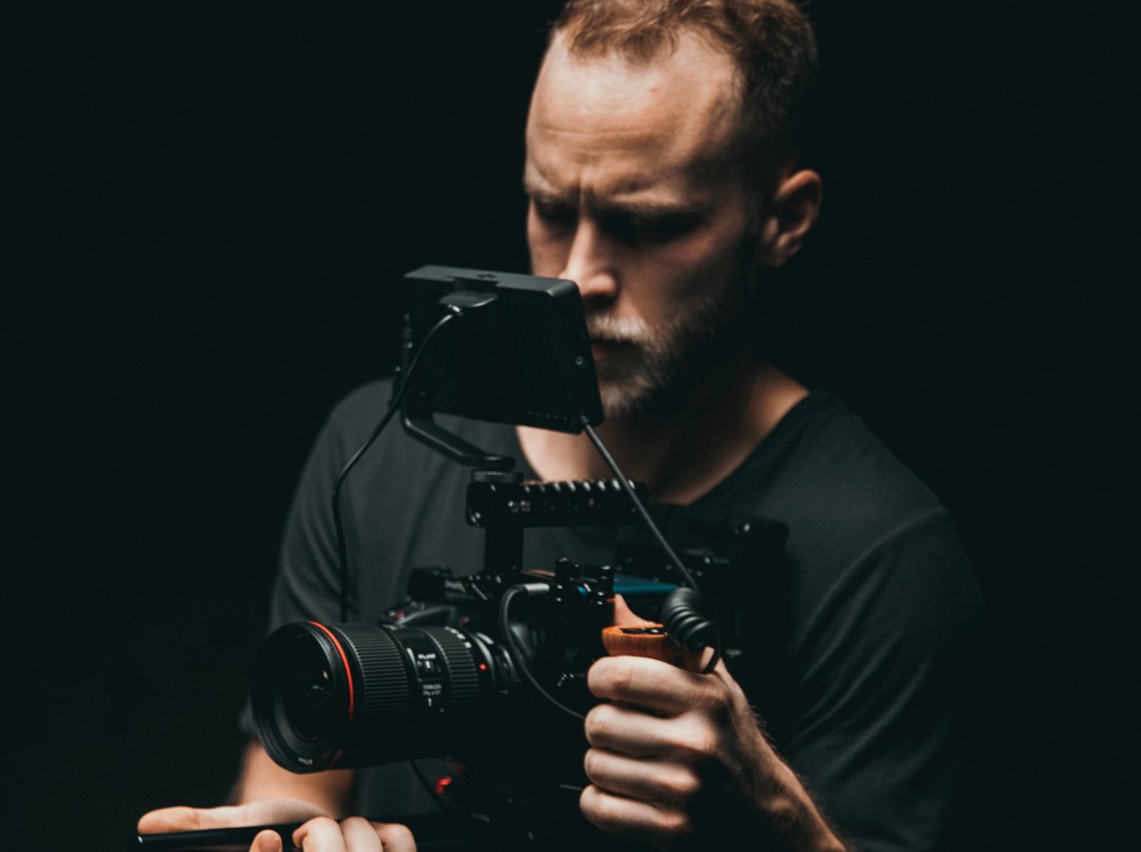 A man is holding a camera in his hands in a dark room.