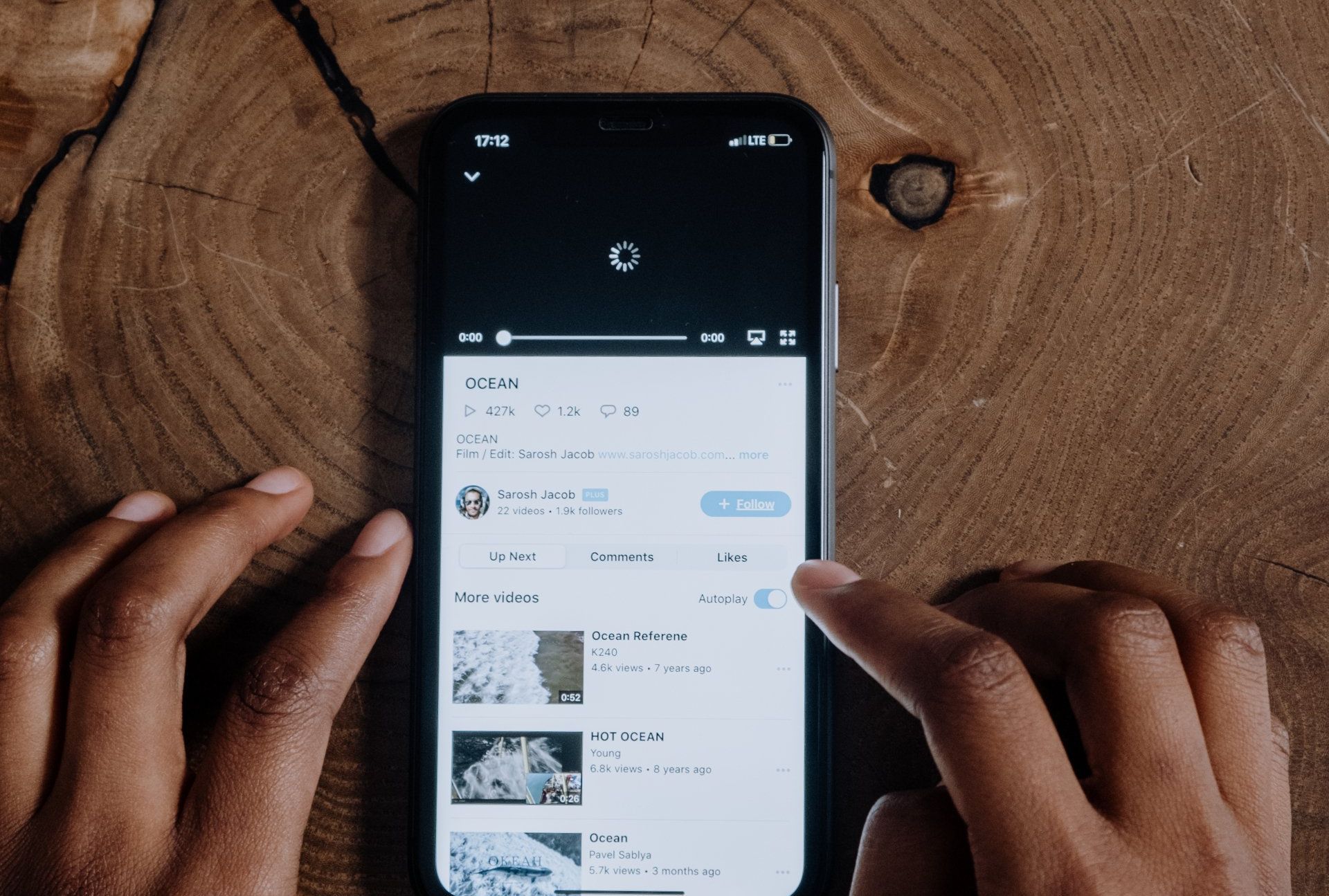 A person is using a cell phone on a wooden table.