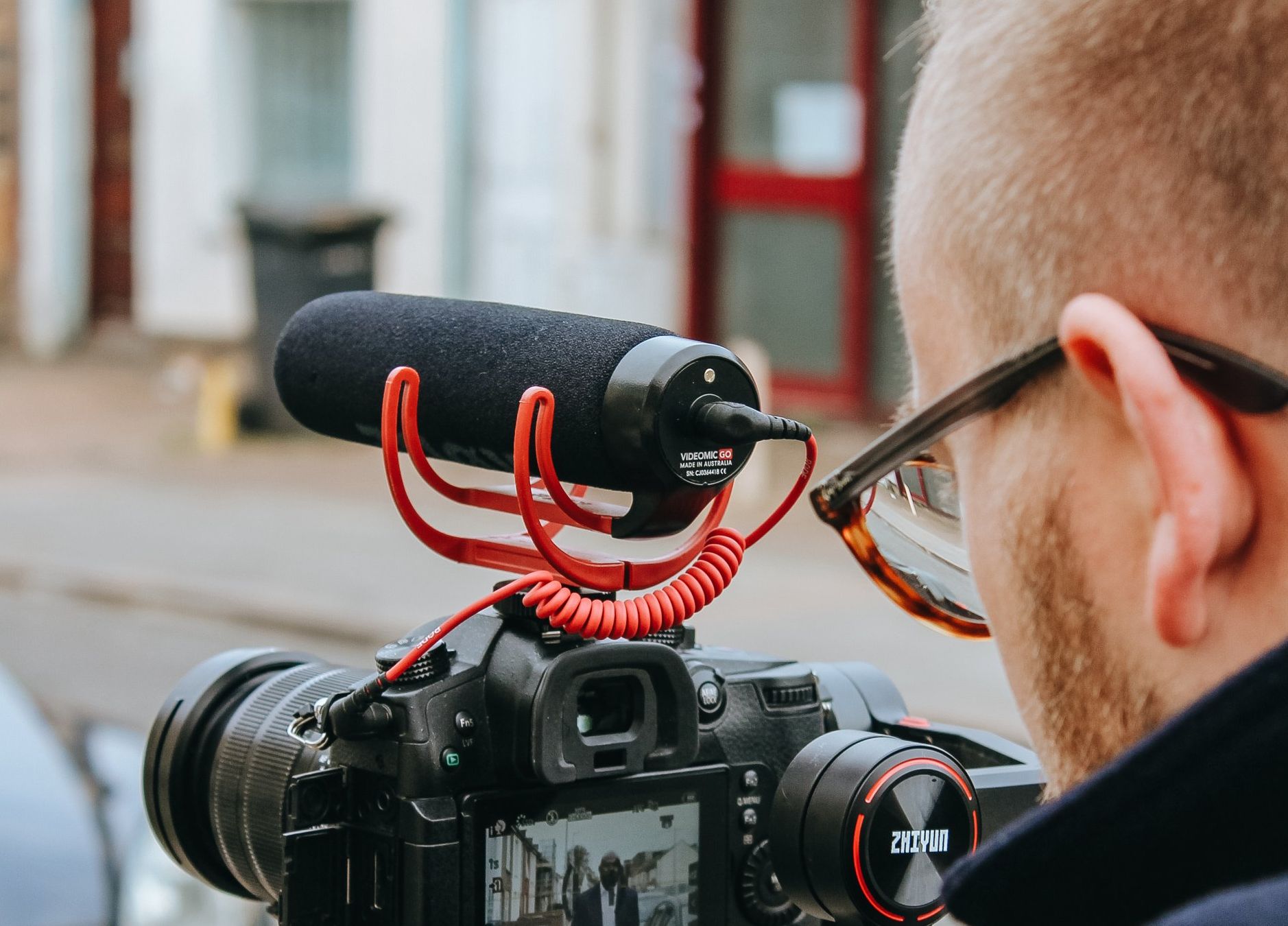 A man wearing glasses is looking at a camera with a microphone attached to it.