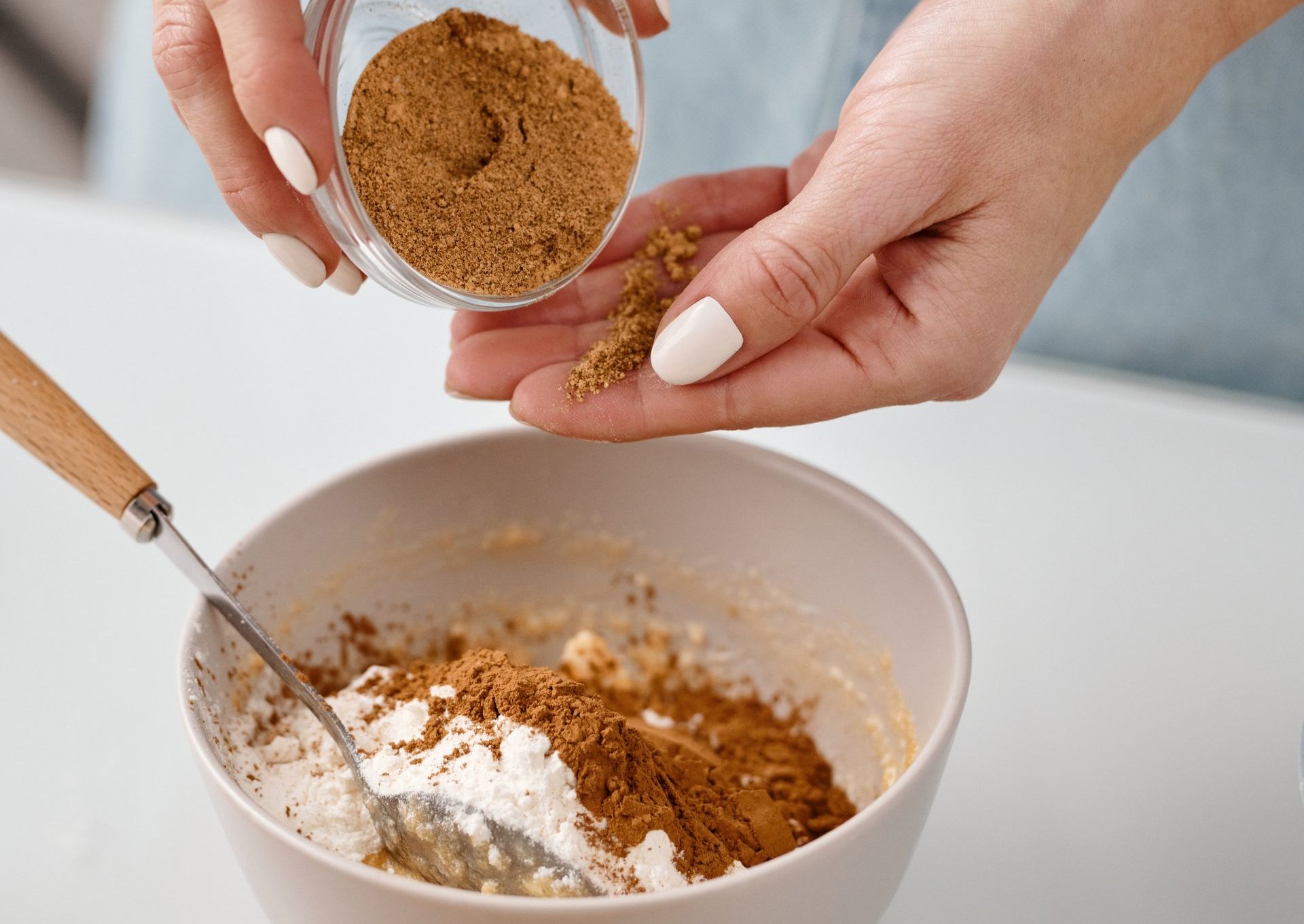 A person is pouring brown sugar into a bowl of flour.