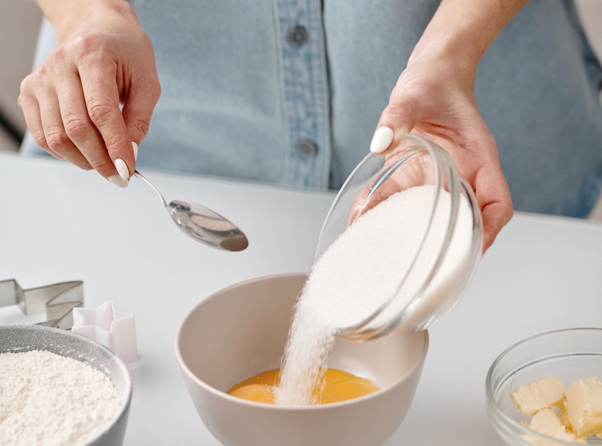 A woman is pouring sugar into a bowl of liquid with a spoon.