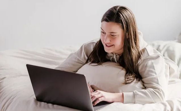 A woman is laying on a bed using a laptop computer.