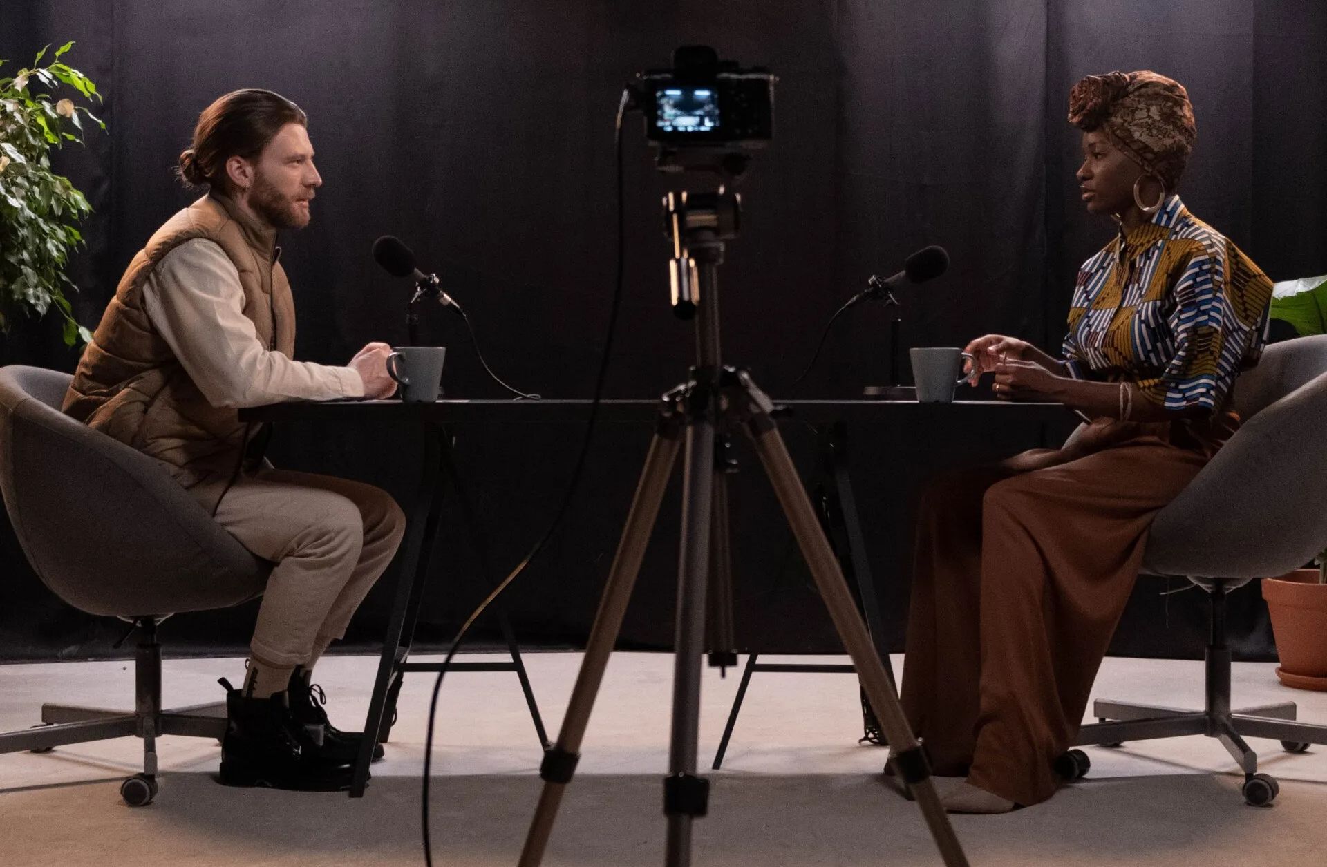 A man and a woman are sitting at a table talking into microphones.