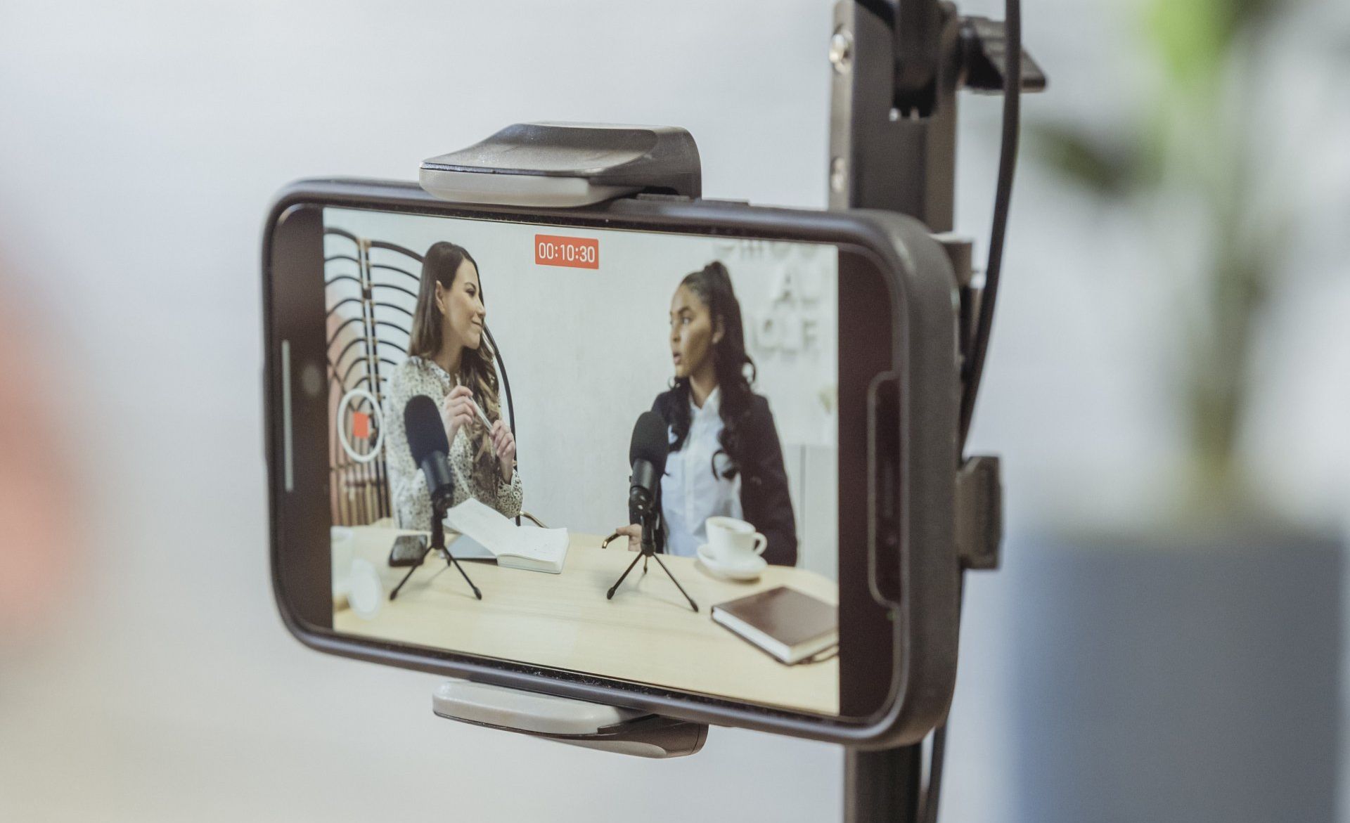 A cell phone is being used to record a video of two women talking into microphones.