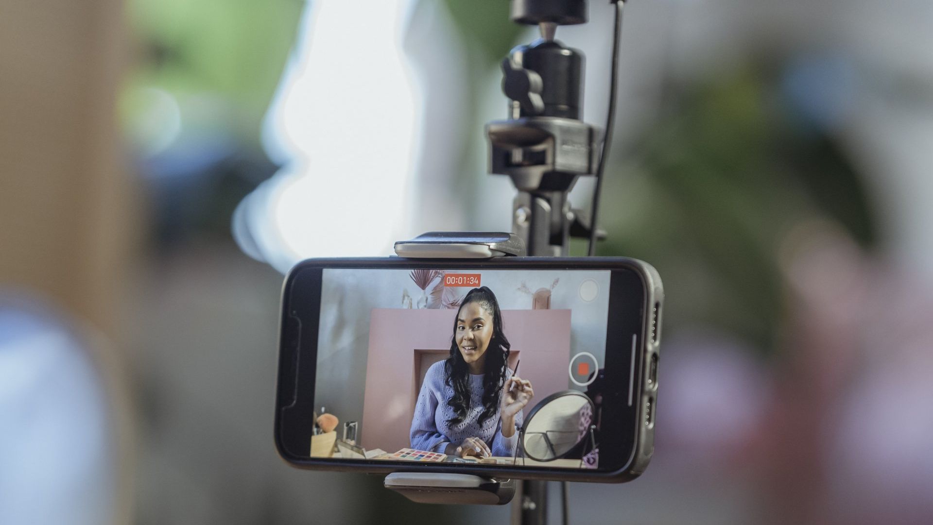 A woman is being filmed on a cell phone on a tripod.