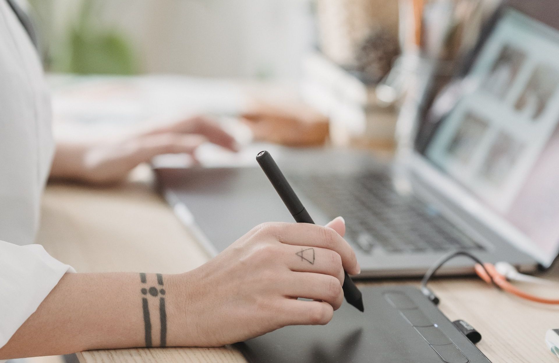 A person is using a pen on a tablet in front of a laptop computer.