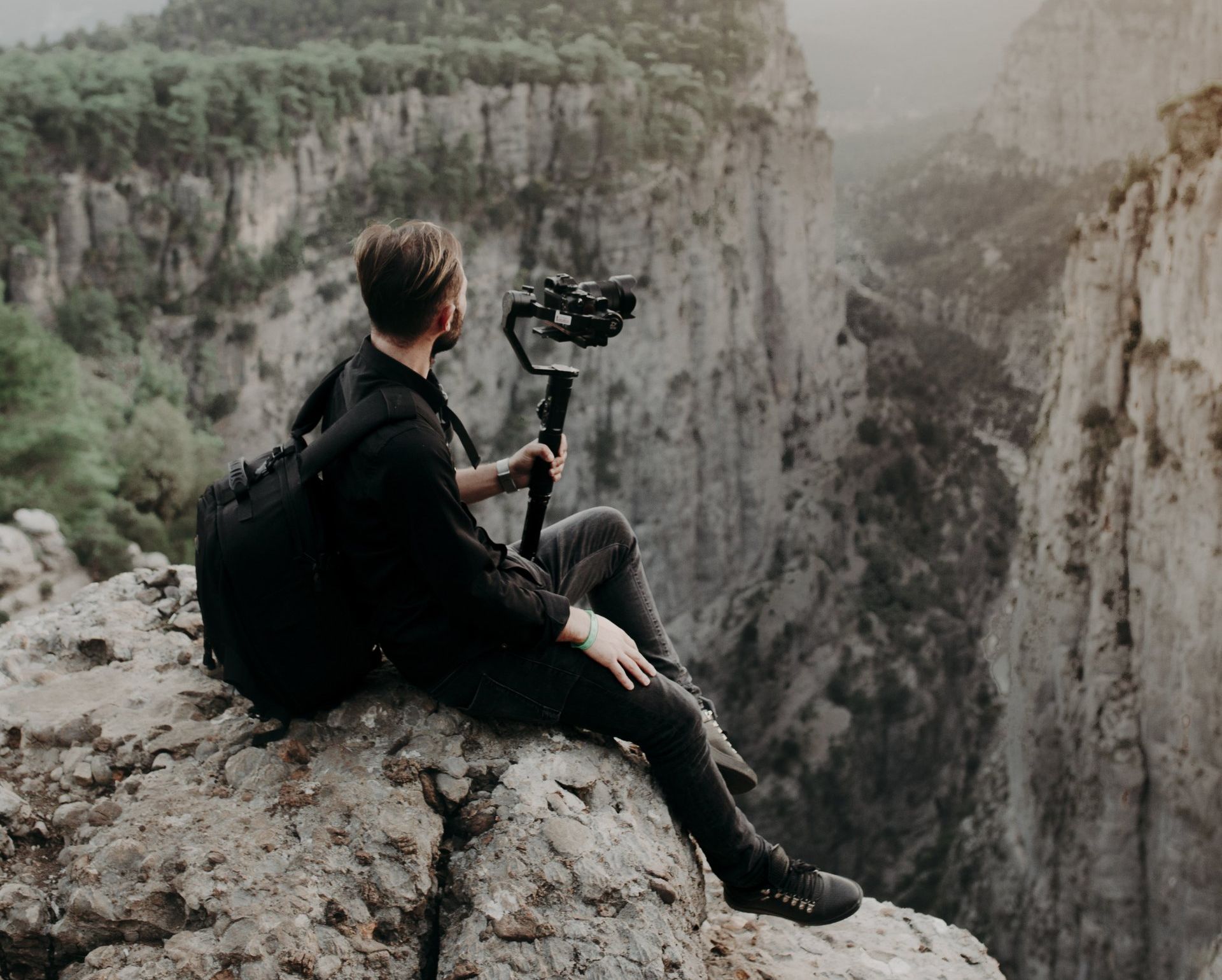 A man is sitting on the edge of a cliff holding a camera.