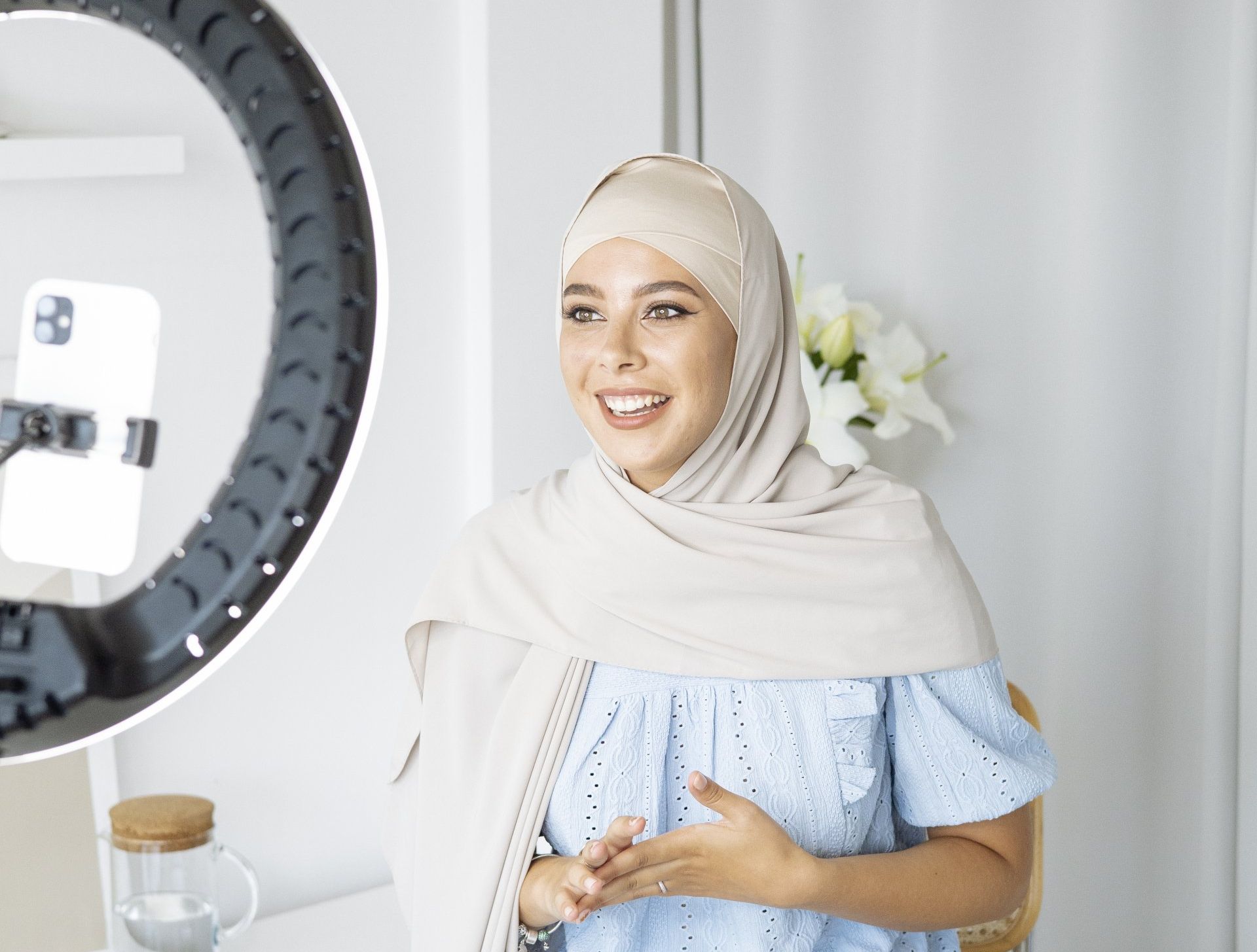 A woman in a hijab is standing in front of a ring light.