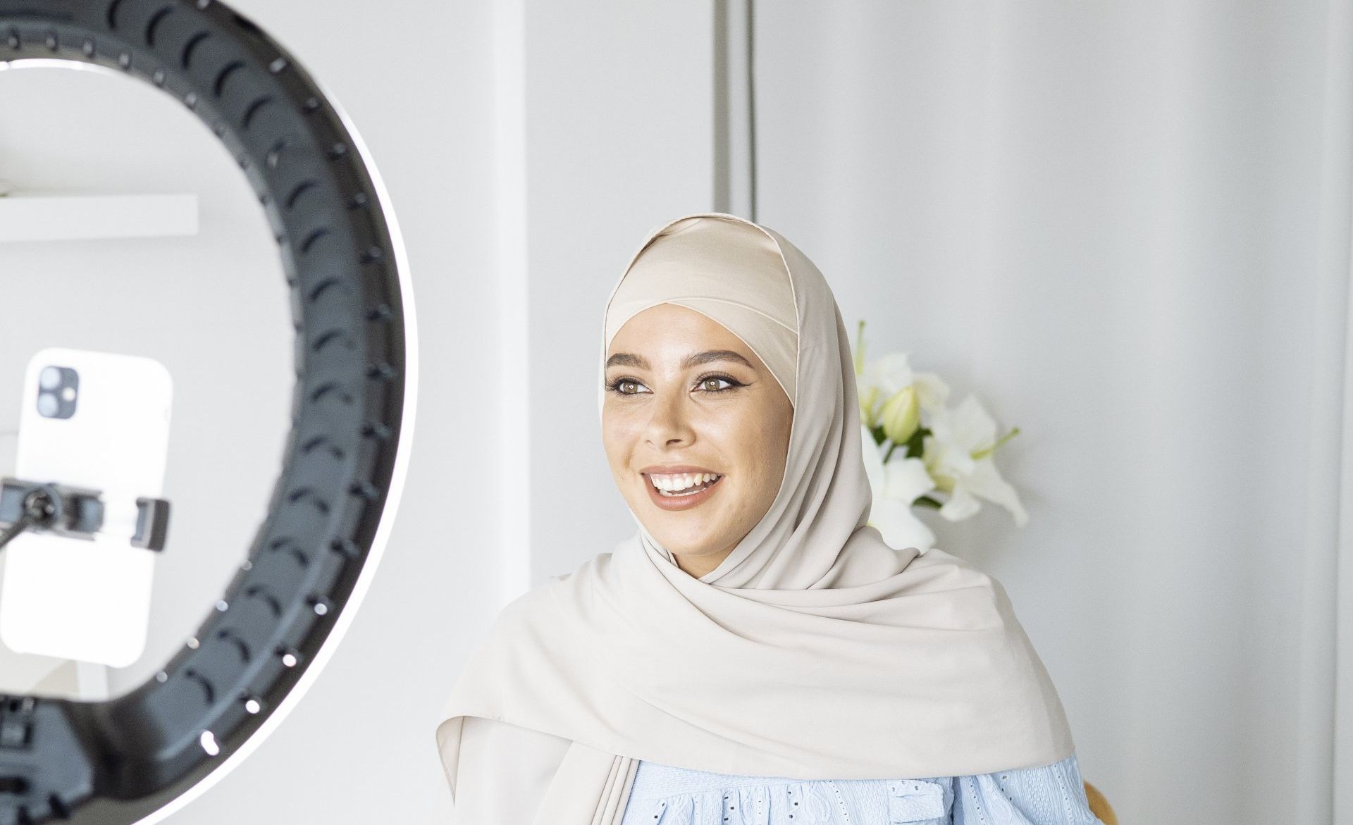 A woman in a hijab is standing in front of a ring light.