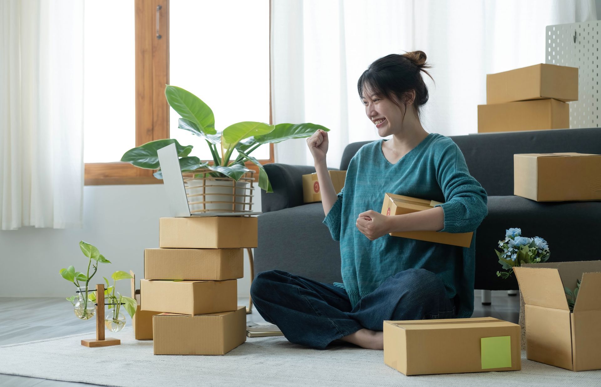 A woman is sitting on the floor in front of a couch surrounded by cardboard boxes.