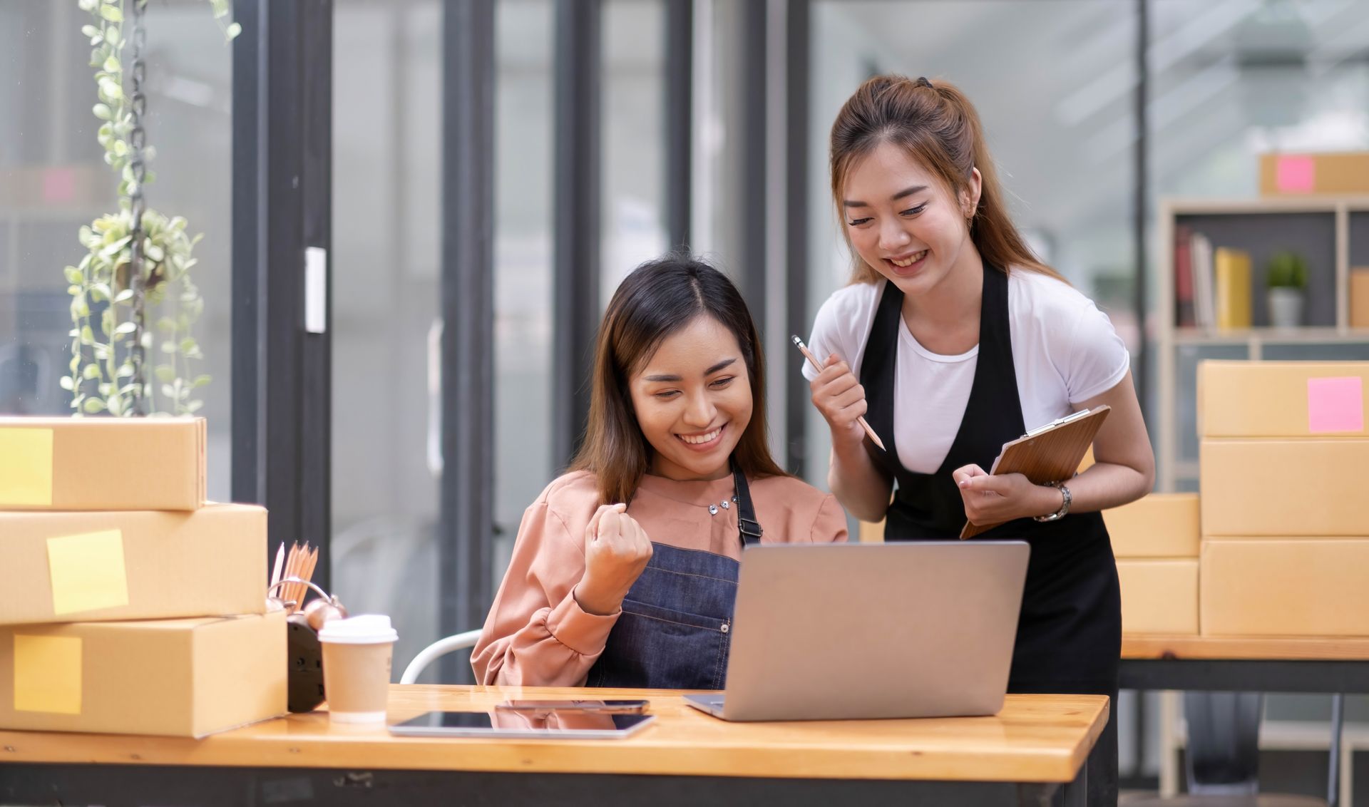 Two women are sitting at a table looking at a laptop computer.