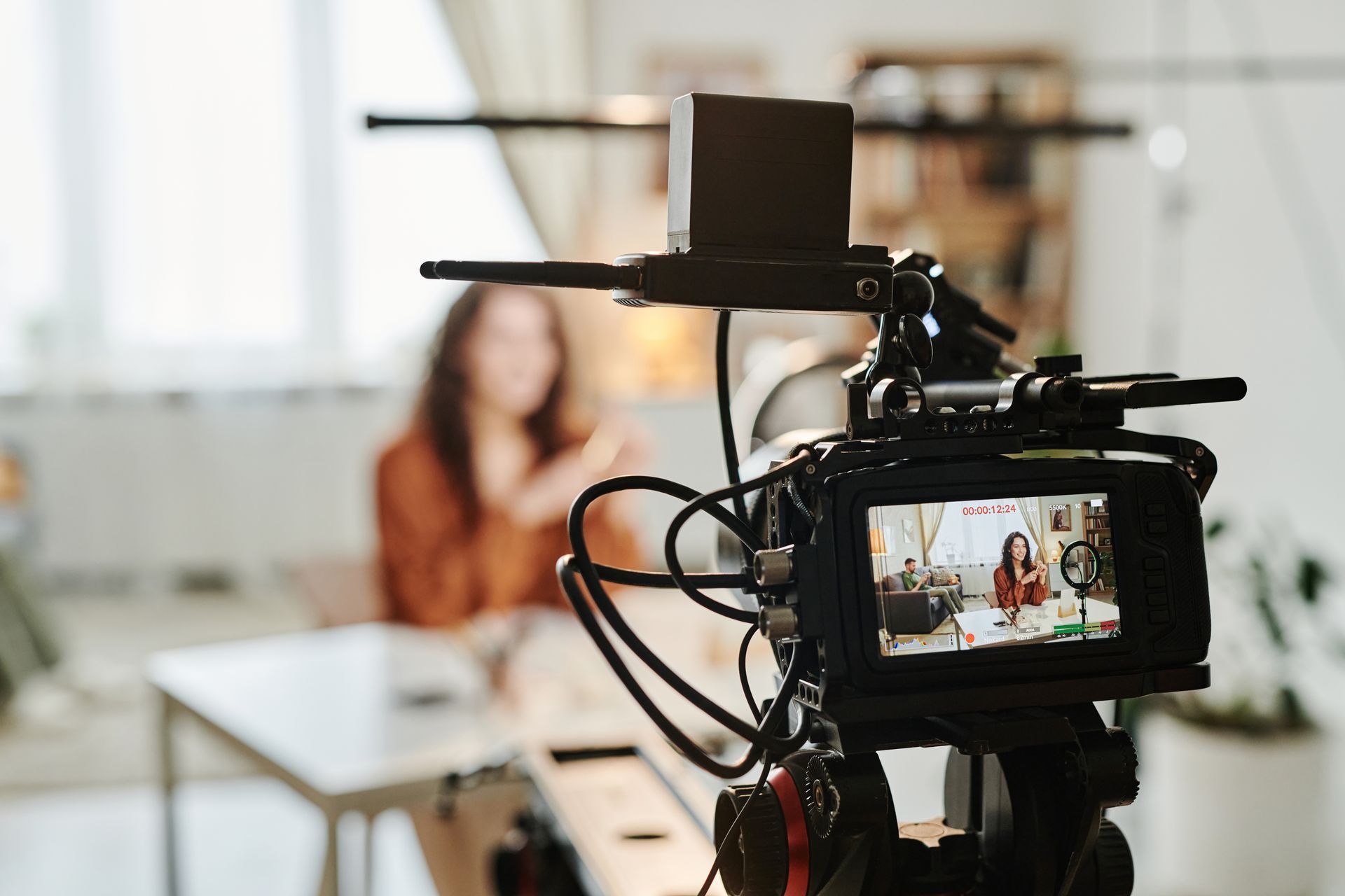 A video camera is recording a woman sitting at a table.