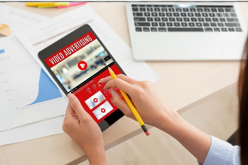 A woman is holding a tablet with a video advertising screen on it.