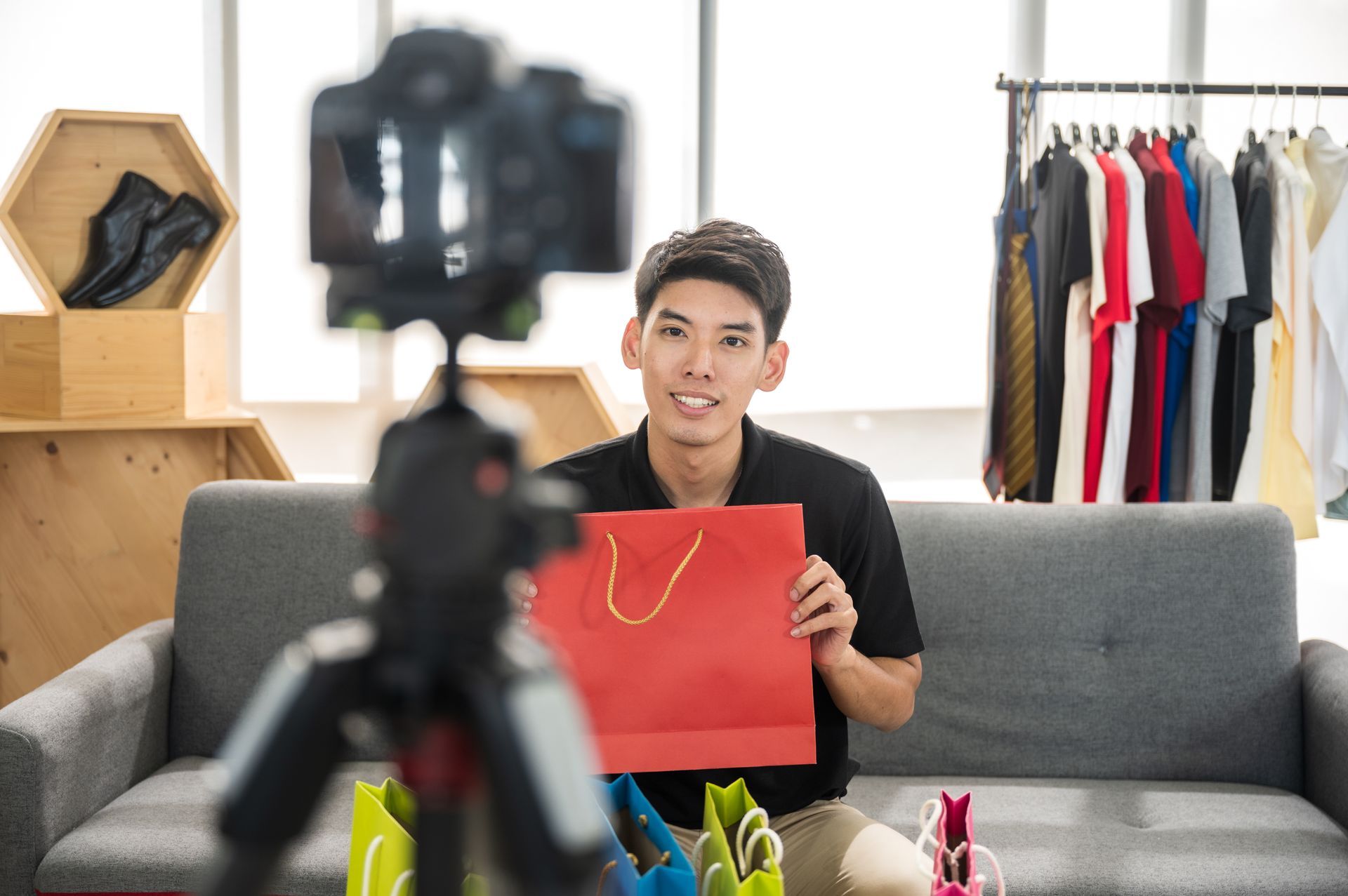 A man is sitting on a couch holding a shopping bag in front of a camera.