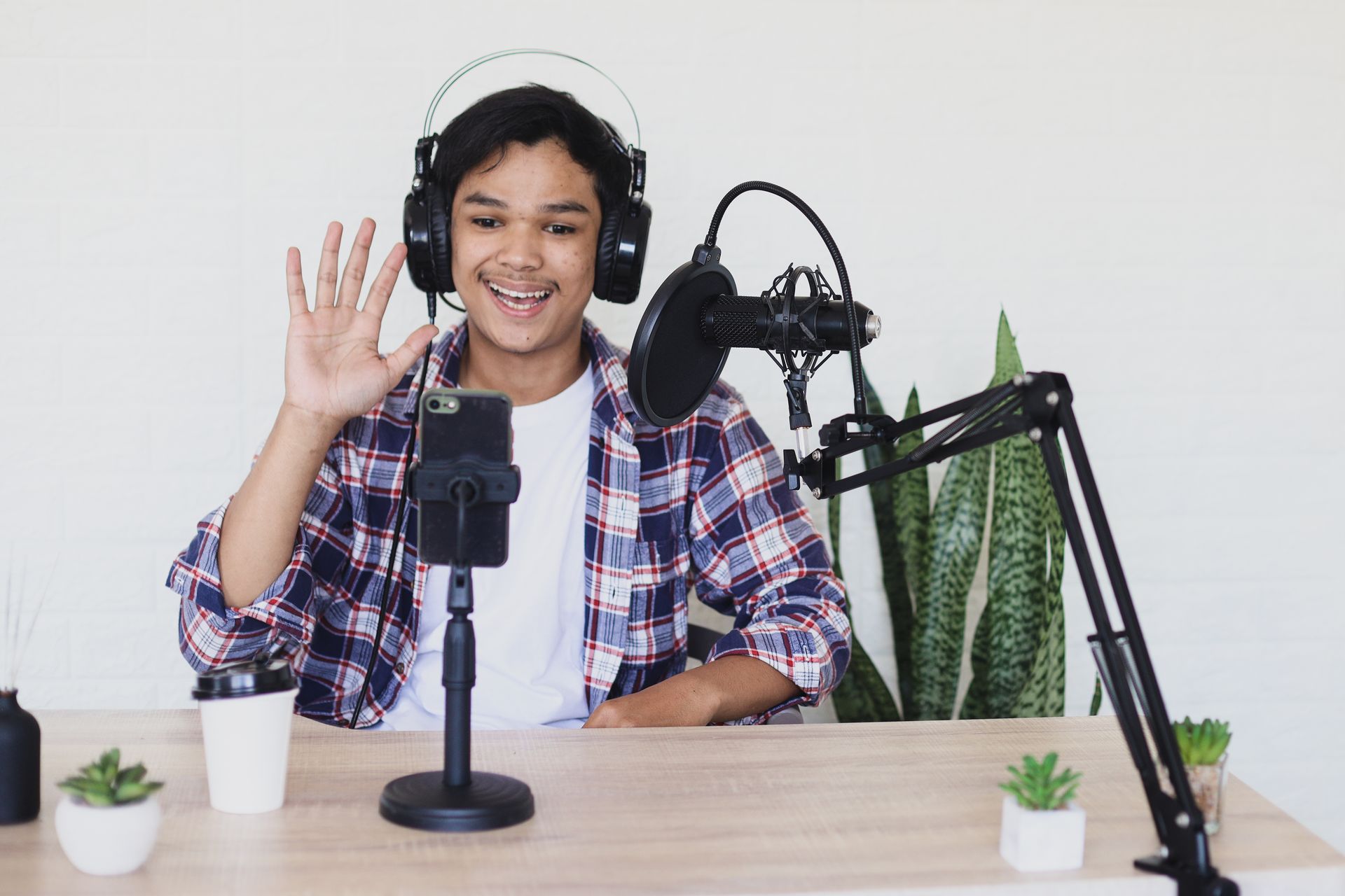 A man wearing headphones is sitting at a table with a microphone and a cell phone.