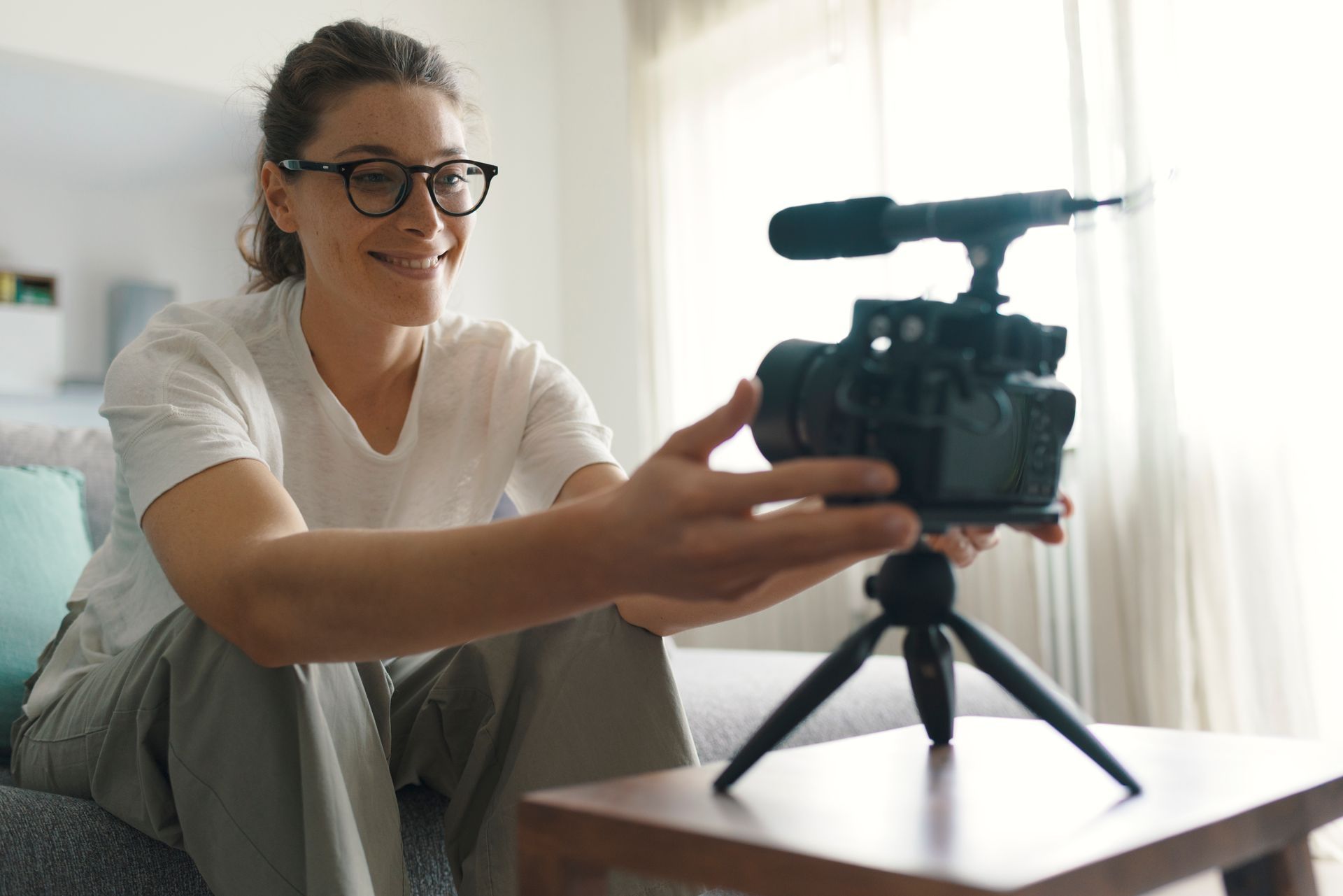 A woman is sitting on a couch holding a camera on a tripod.