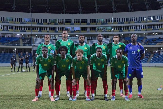Soccer team in green jerseys and red socks poses on a field in front of a stadium.