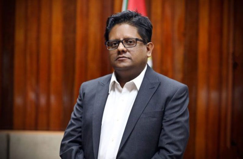 Man in suit and glasses stands in front of a wooden panel.