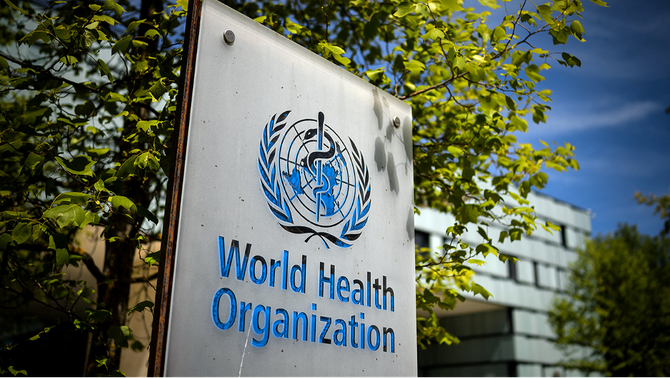 Sign with World Health Organization logo in front of a building with trees.