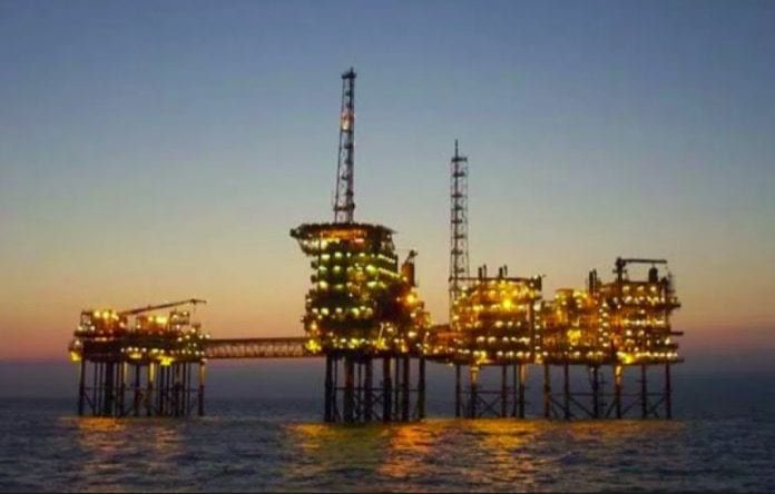 Oil rig platform lit up at dusk, offshore in the ocean.