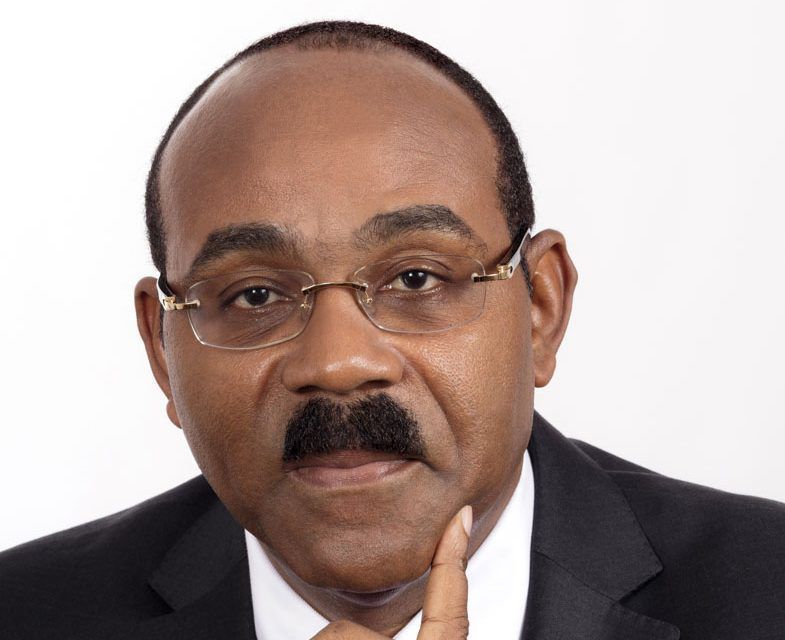 Man in suit, wearing glasses, and touching chin, looking directly at the viewer.