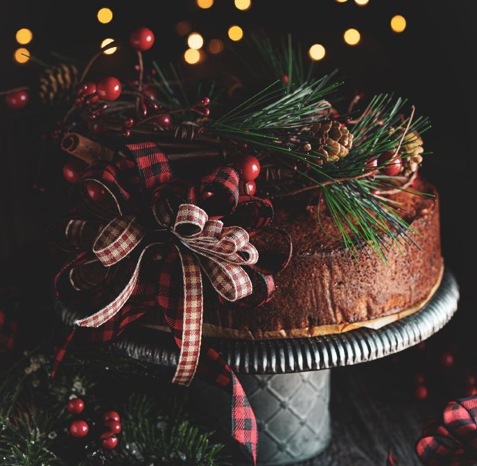 Christmas cake with plaid bow and festive decorations on a silver cake stand.