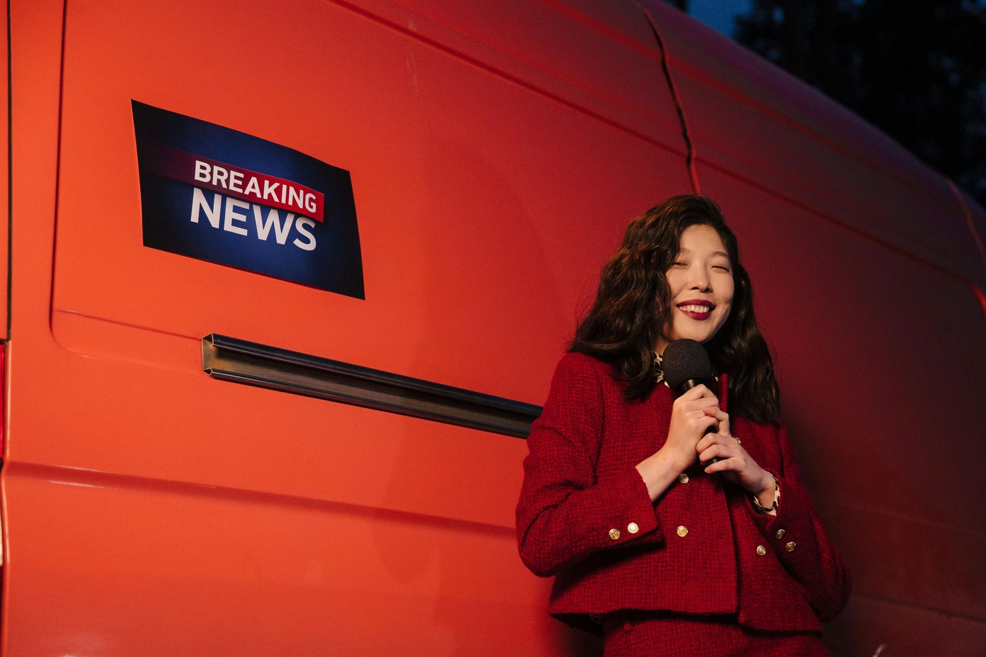 Woman in red suit speaking into a microphone in front of an orange truck with a 