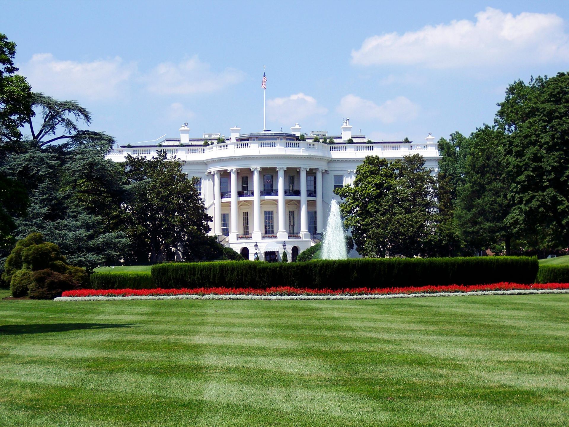 White House with green lawn and red flowers in a sunny setting.