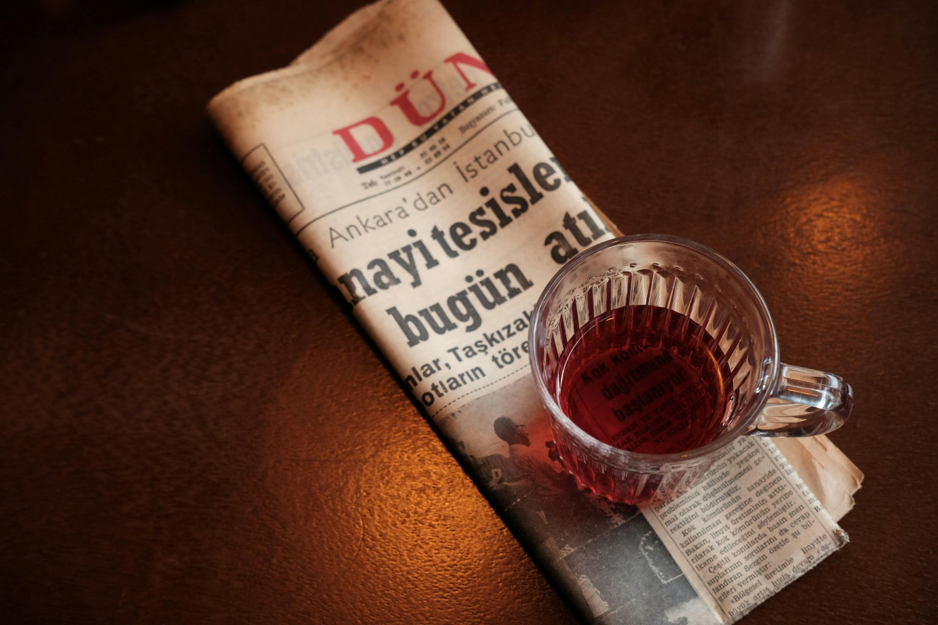 Newspaper with Turkish text, a glass of tea on a dark wooden surface.