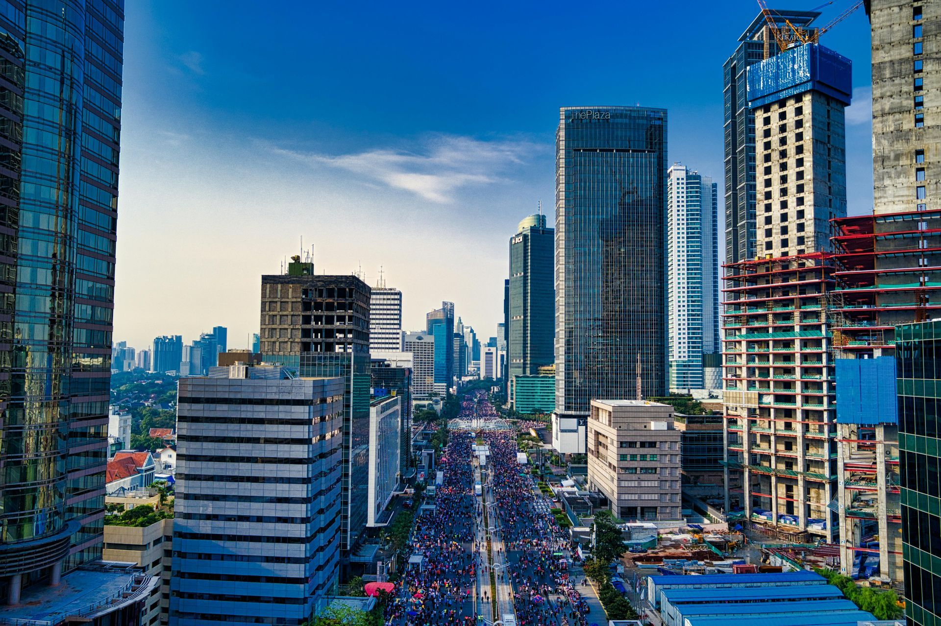City street lined with tall buildings under a blue sky, full of traffic.
