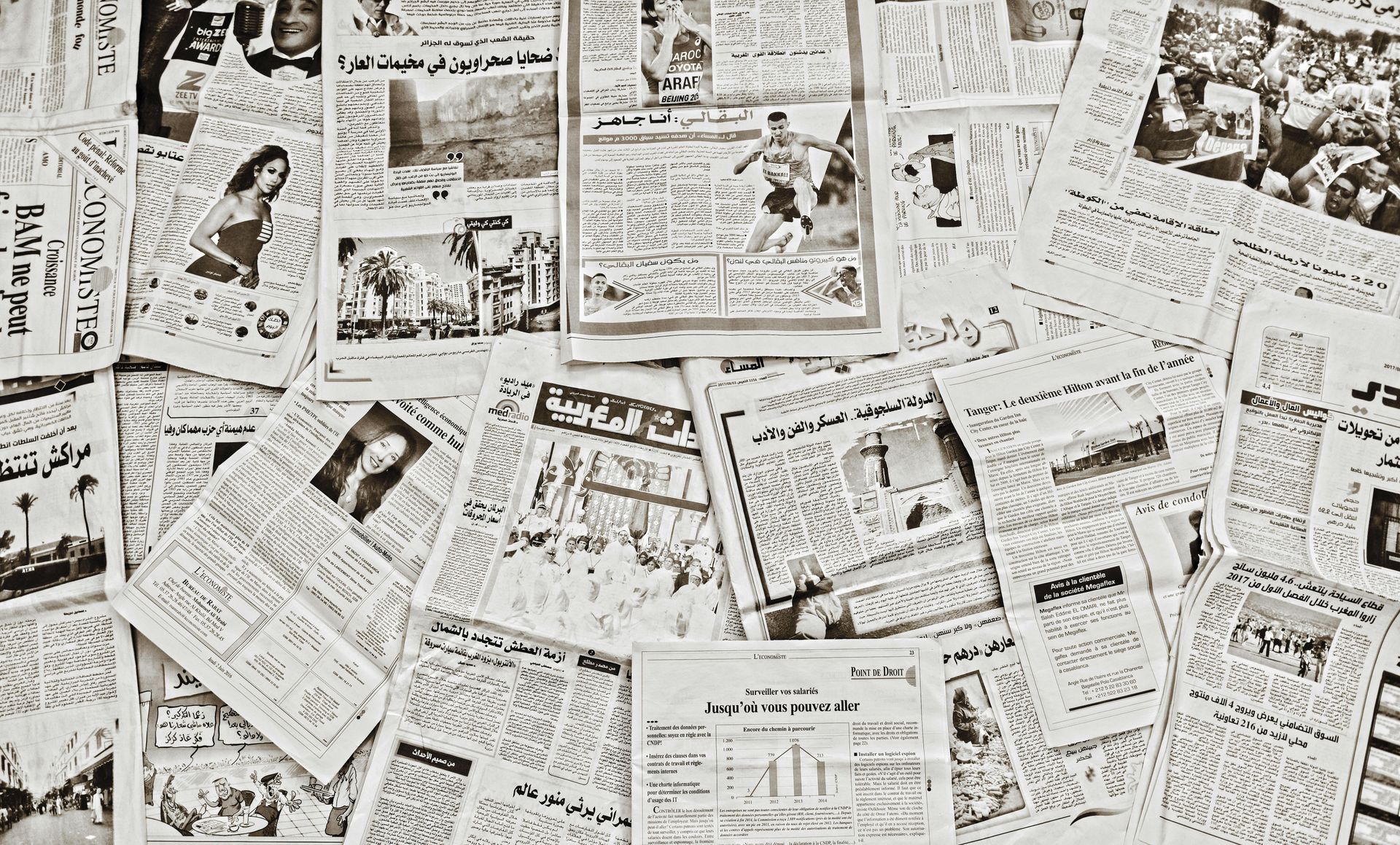 Pile of open newspapers; articles and photos visible, creating a textured, newsprint background.