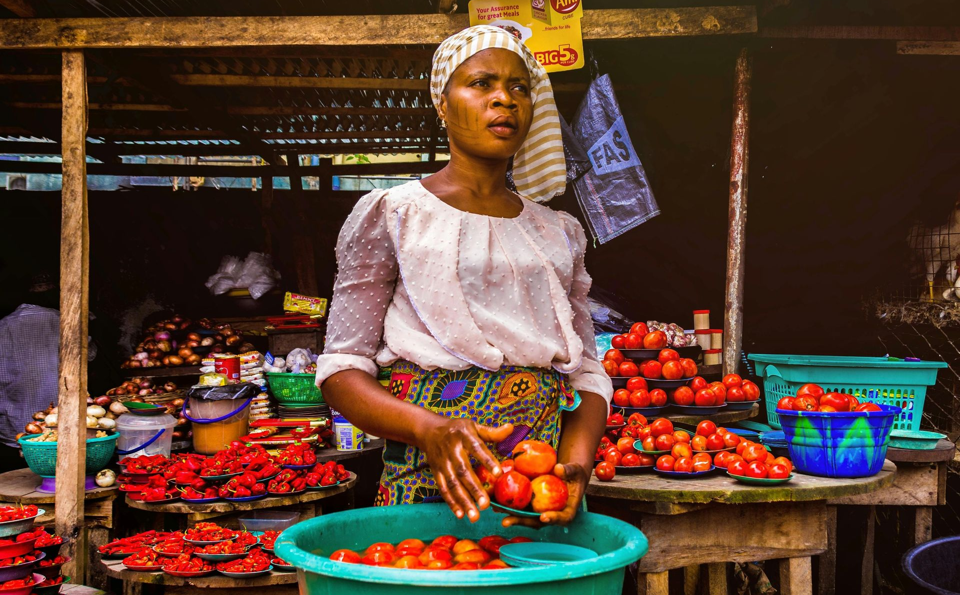 Woman at a market stall selling tomatoes, sorting them into a bowl. Tomatoes are red.