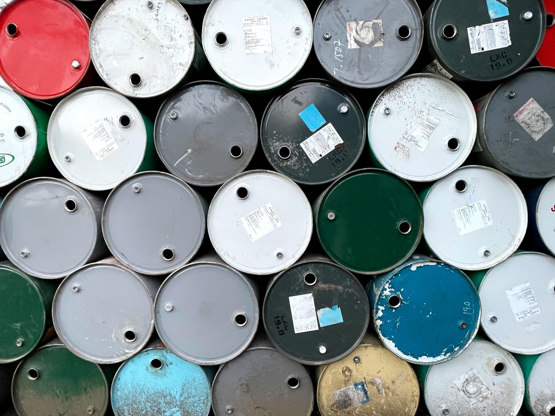 Stacked, colorful metal barrels; some with labels and holes.