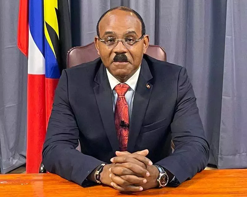 Man in a suit sitting at a desk, the flag of Antigua and Barbuda visible behind him.
