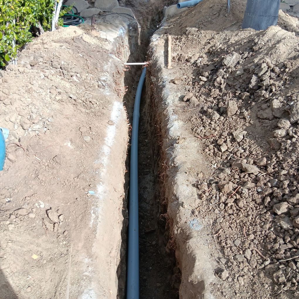 Deep narrow trench in soil with a black pipe running down the center outdoors