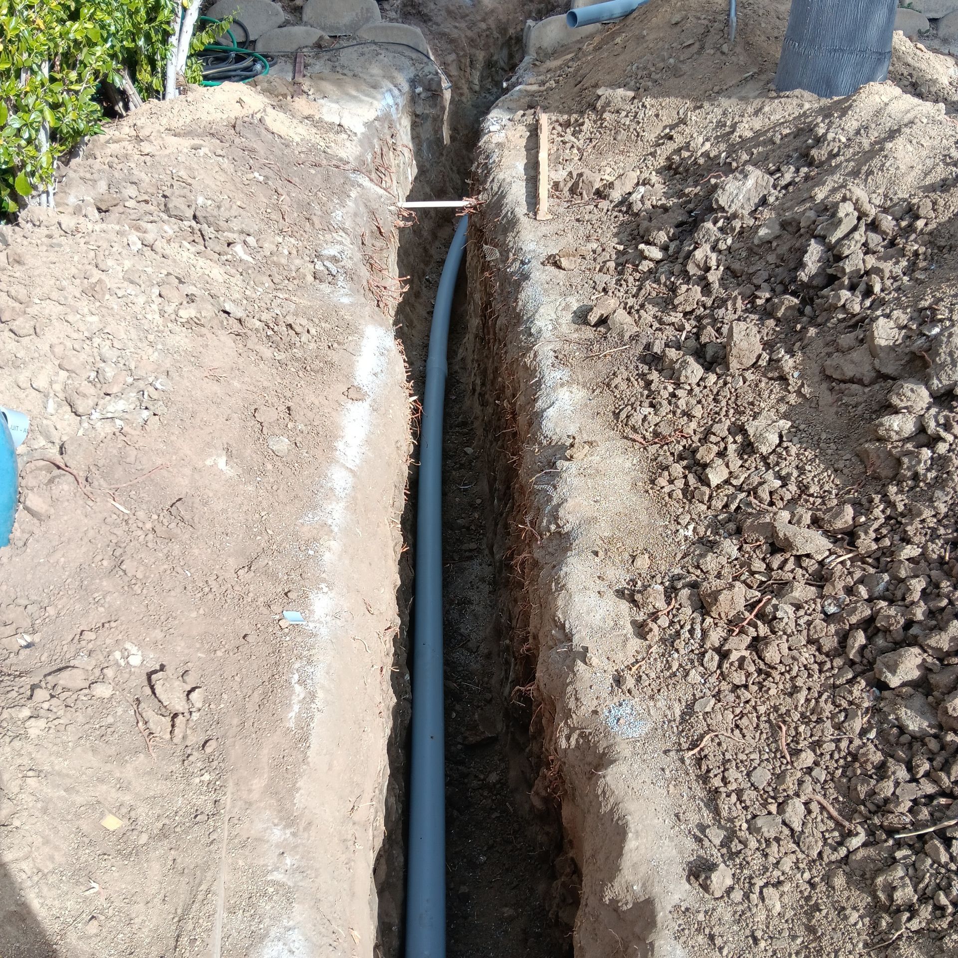 Narrow trench in dirt with a black pipe laid along the center at a construction site