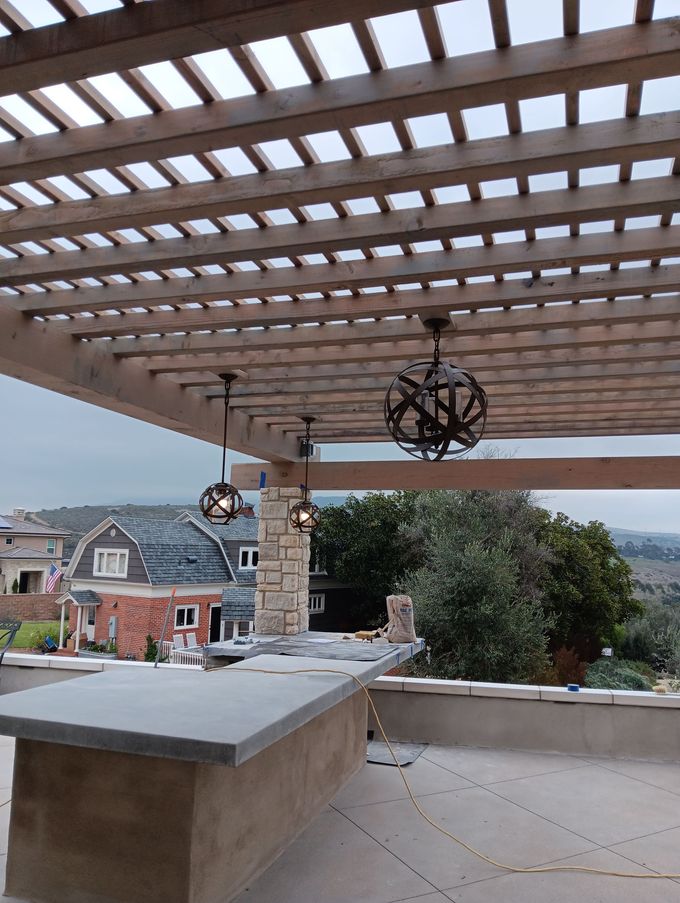 Outdoor patio with pergola, hanging lanterns, stone counter, and hillside view of houses and trees