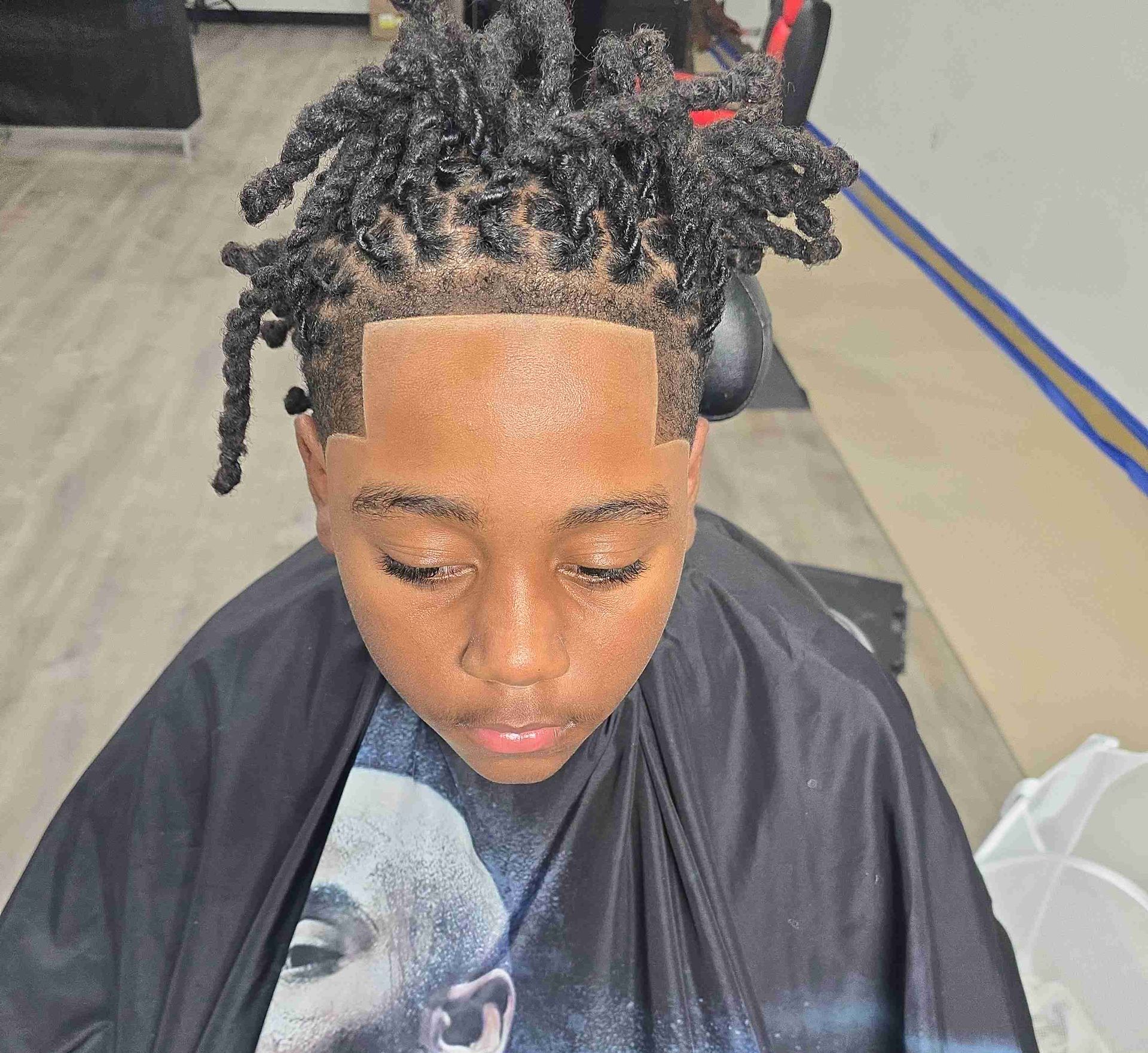 A young man with dreadlocks is getting his hair cut in a barber shop.