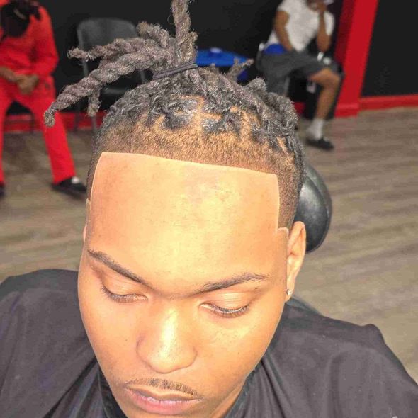 A man with dreadlocks is getting his hair cut at a barber shop.