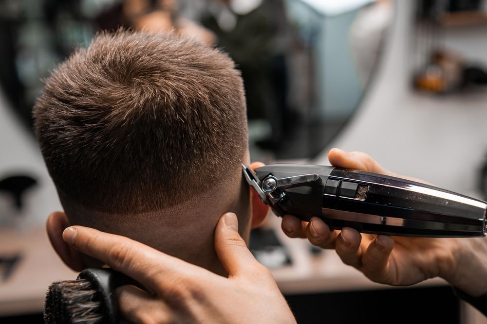A man is getting his hair cut by a barber with a clipper.